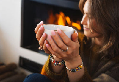 Ein gemütlicher Moment vor dem Kamin, während man eine Tasse Tee trinkt und Trollbeads-Herbstschmuck trägt.