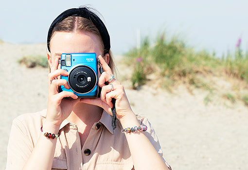Model mit Polaroidkamera am Strand, sie trägt Armbänder mit Trollbeads Schmuck