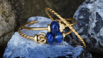 Trollbeads vergoldete Armspange mit blauen Edelsteinen und goldenen Beads auf einem Felsen
