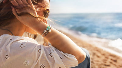 Model am Strand mit Jeans und weißer Blümchen Bluse, sie trägt Schmuck der Kollektion Schätze der Gezeiten