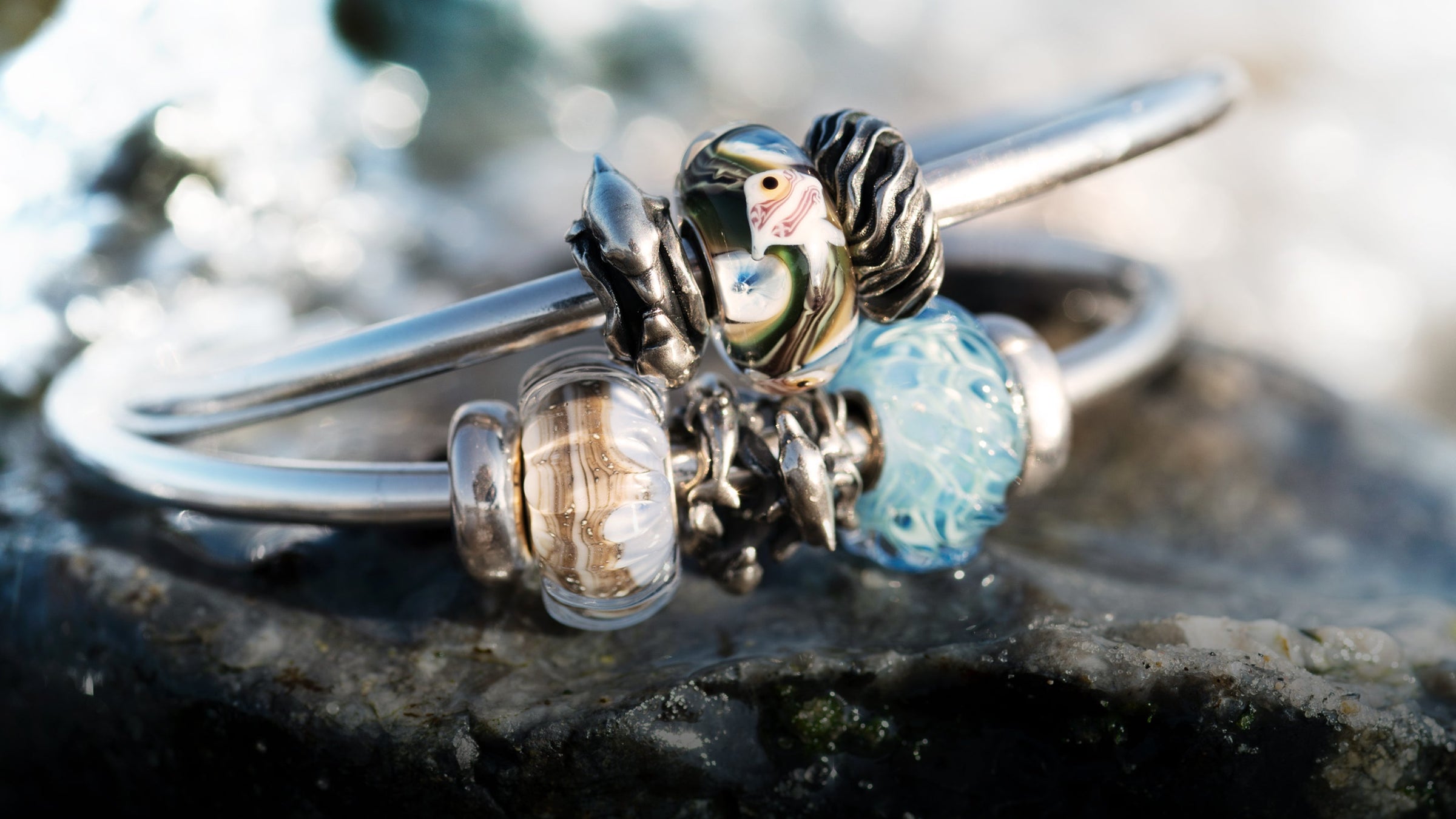 2 Silberarmbänder, die auf einem nassen Felsen liegen, mit Glasbeads und 4 silbernen Spacern