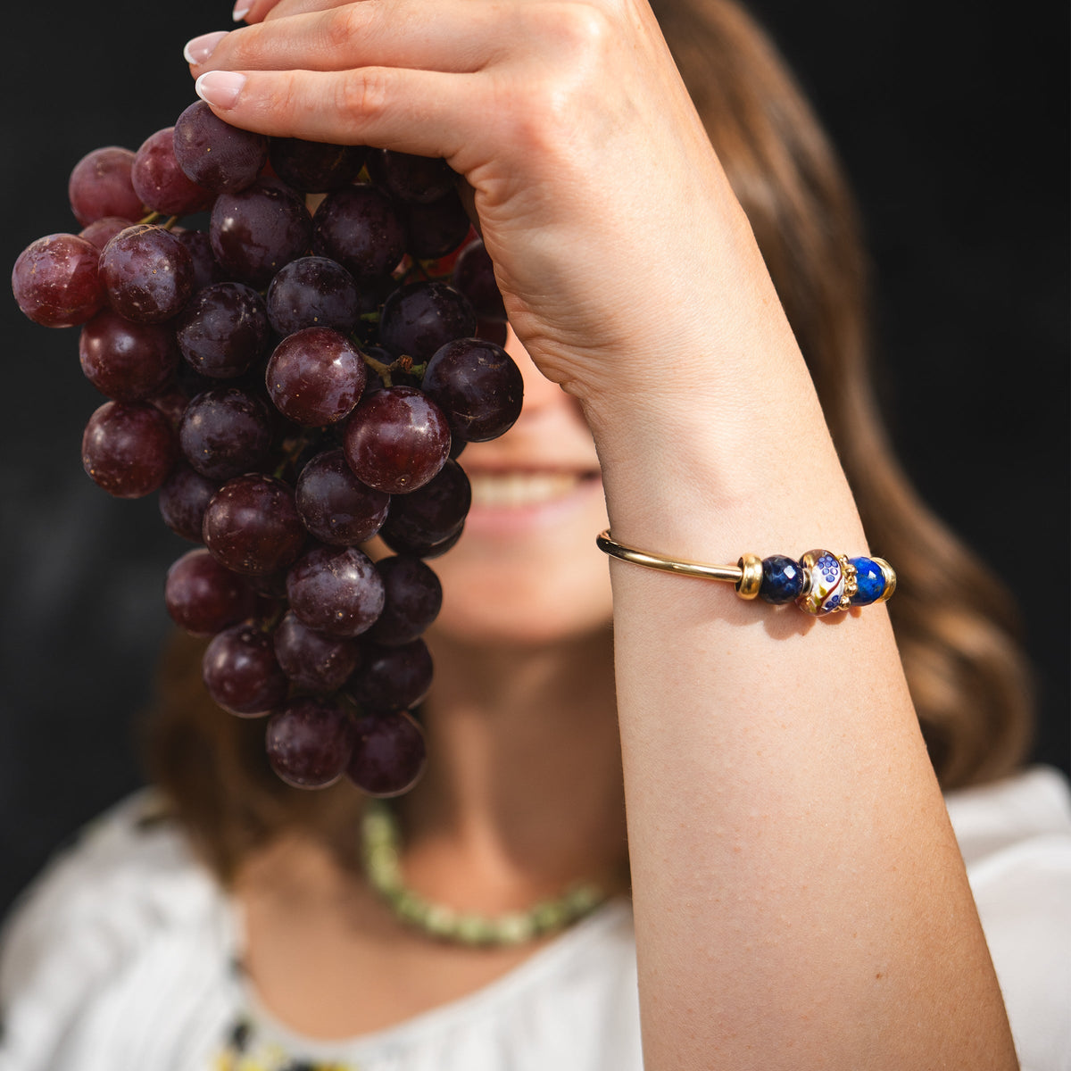 Model mit Trauben in der Hand, das eine vergoldete Armspange mit Beads trägt