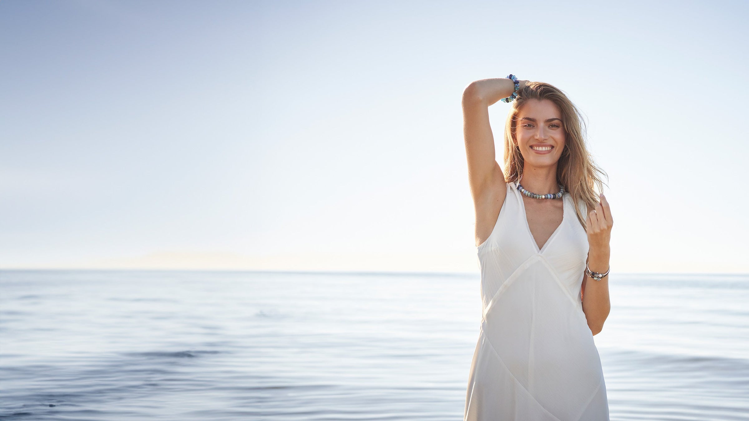 Ein Model trägt eine Trollbeads Kette und ein Armband und steht lächelnd im Wasser an einem Strand