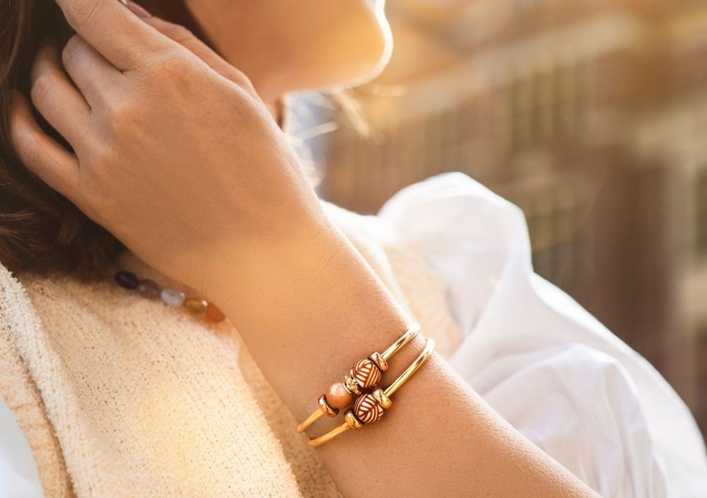 Eine Frau, die einen goldenen Armreif mit Barrel Beads trägt, im warmen Sonnenlicht.