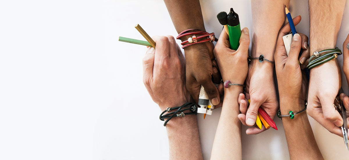 6 Hände, wobei jedes Handgelenk ein Trollbeads-Armband und Beads trägt. Sie haben Künstlerbedarf in den Händen für den People's Bead Design Wettbewerb