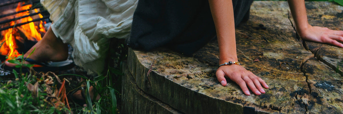 Ein Model, das ein Armband mit Edelstein und Silebrbeads trägt, während es neben einem Lagerfeuer sitzt