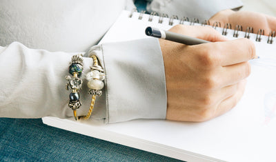 Schreibendes Modell trägt zwei mit Beads verzierte Trollbeads Armspangen
